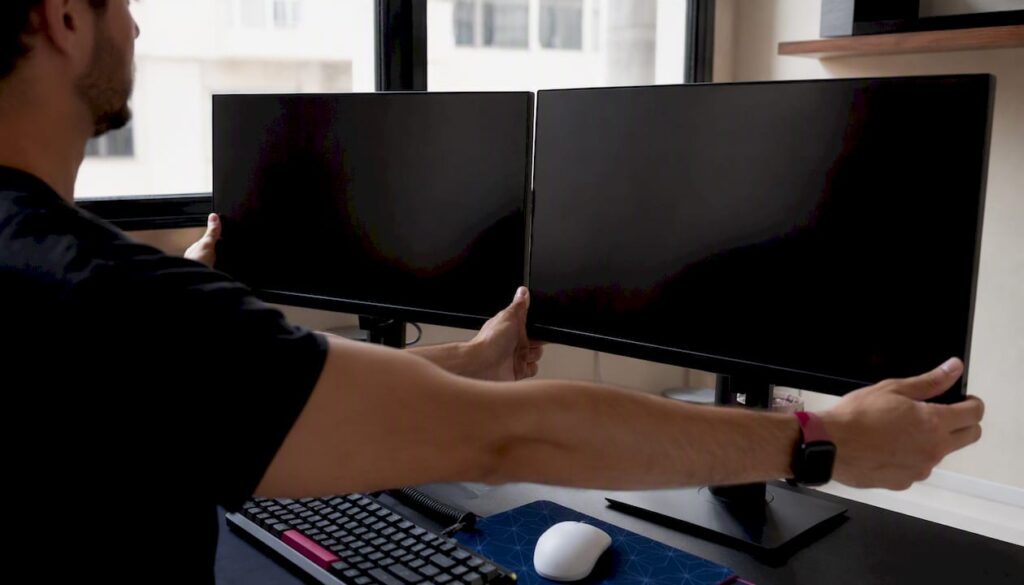 Hands arranging dual monitors for trading comparison
